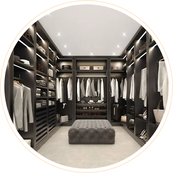 Walk-in closet with dark shelving, white shirts on racks, shoes and bags on display, center tufted ottoman.