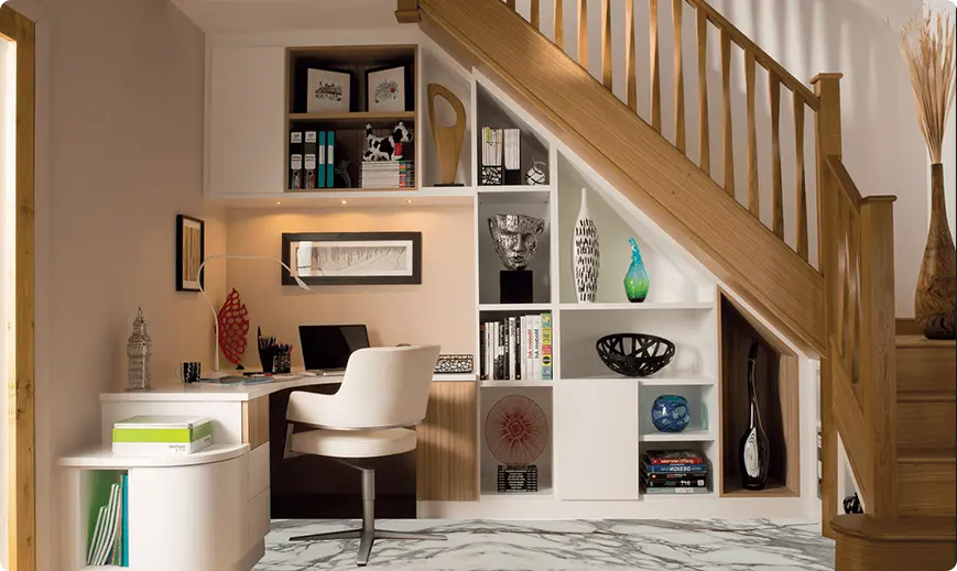 Home workspace under a staircase with built-in shelves, desk, and white chair in a modern room